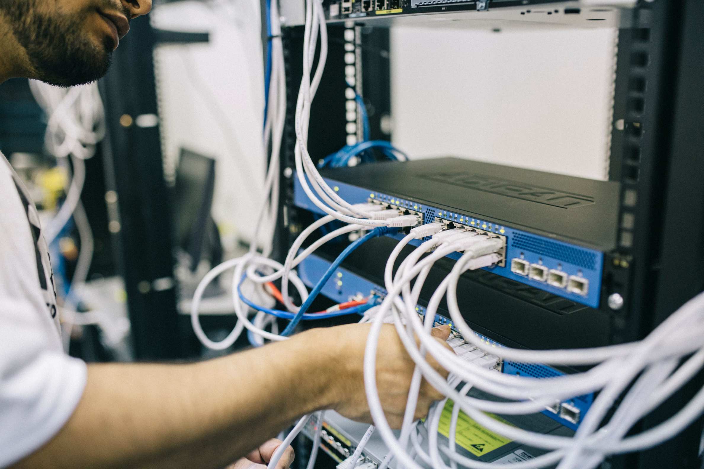 Wide view of a server room aisle with network cabling, IT professional configuring Ethernet cables in a server rack
