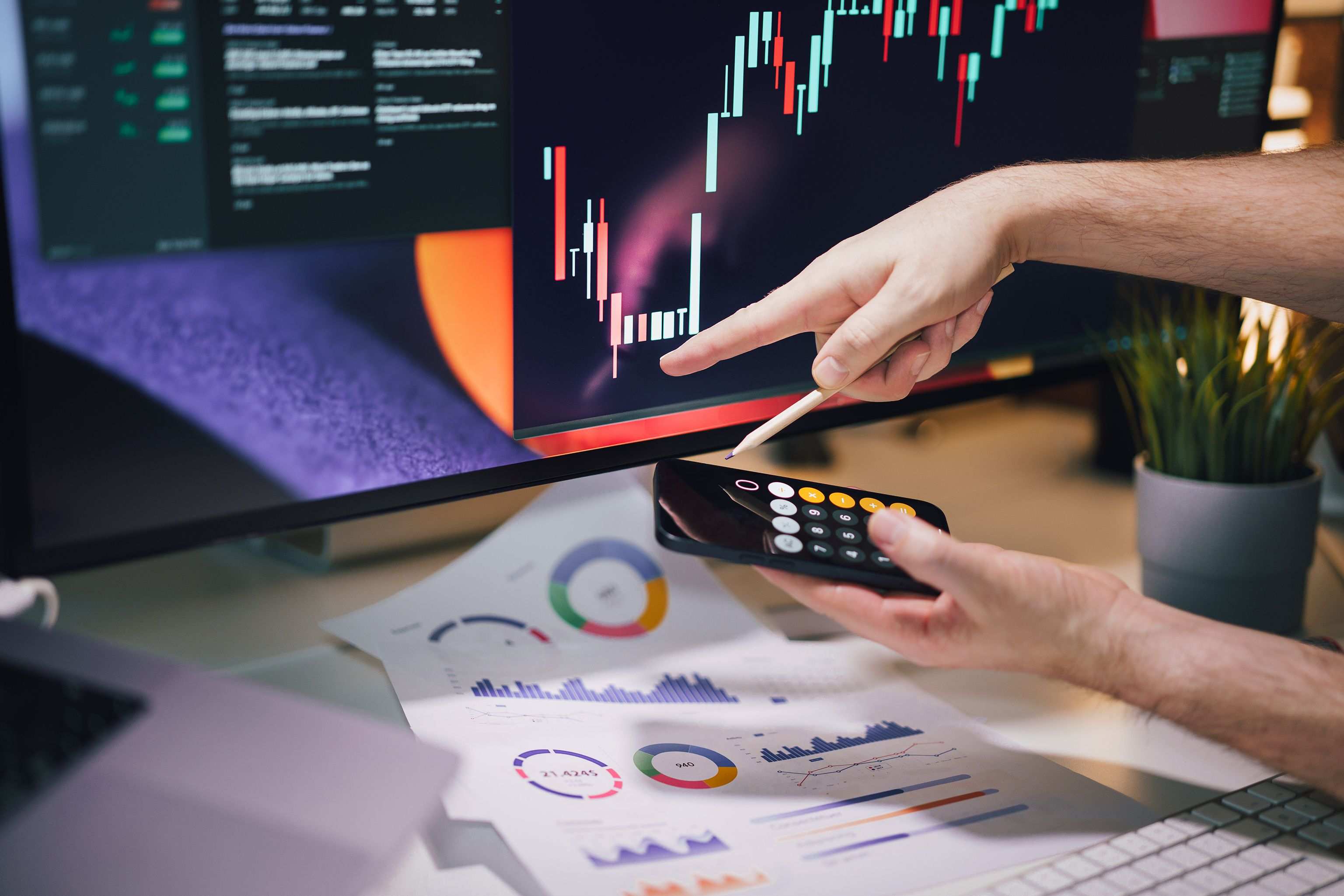 Office desk with monitors showing data charts, hands analyzing data on monitor